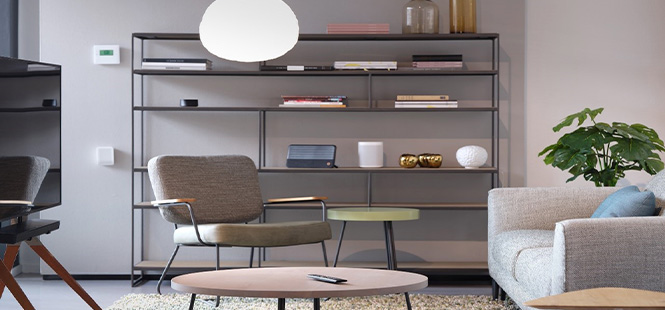 Ein Wohnzimmer mit einem Bücherregal, einem Stuhl, einem Sofa und einem runden Tisch. Auf dem Tisch liegt ein Telefon.