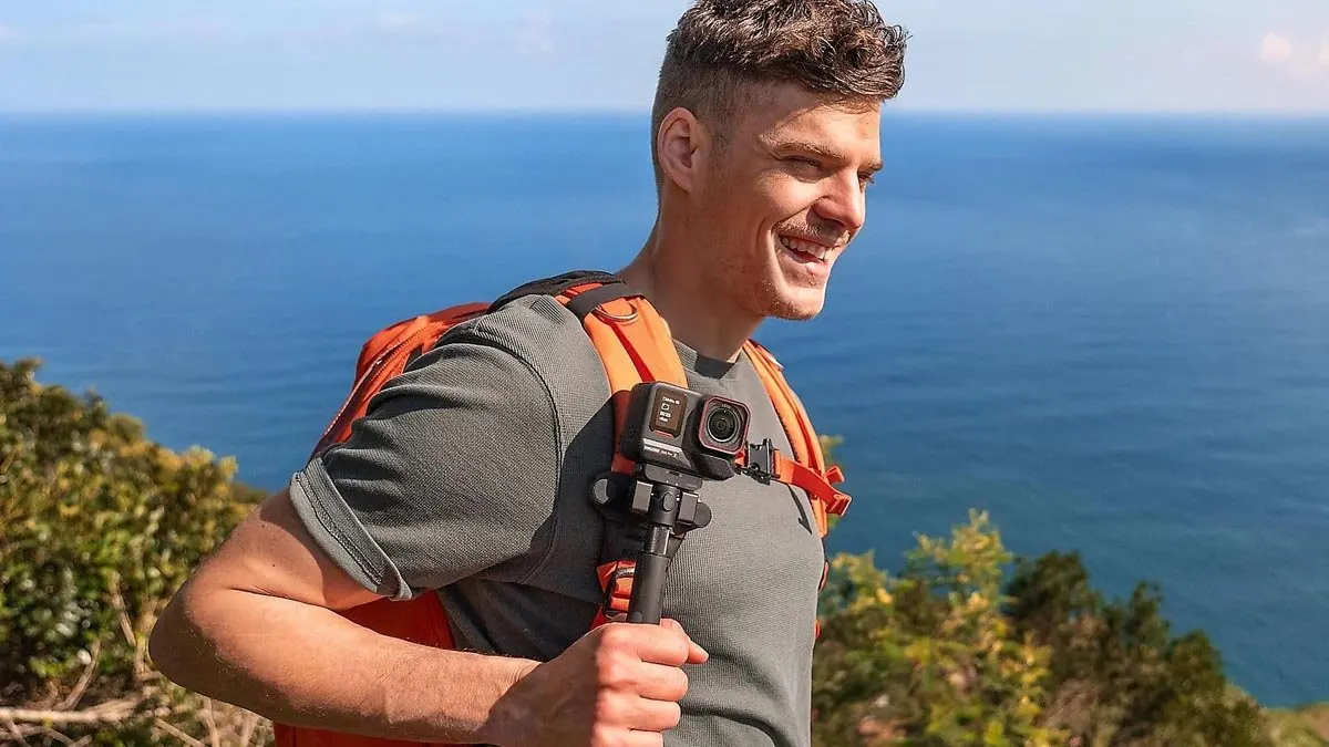 Ein Mann trägt die Action-Cam Insta360 Ace Pro 2 an einem Selfie-Stick beim Wandern am Meer.