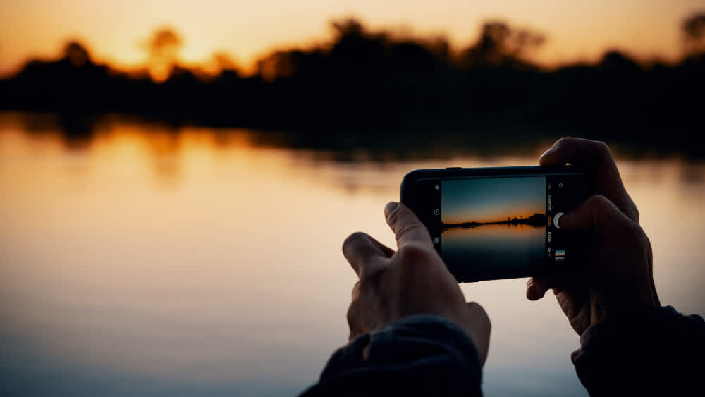 Eine Person filmt den Sonnenaufgang mit einem Smartphone.