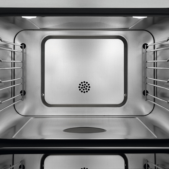 Blick in einen leeren, silberfarbenen Ofen mit Regalen an den Seitenwänden und Lüftungsschlitzen an der Rückwand.