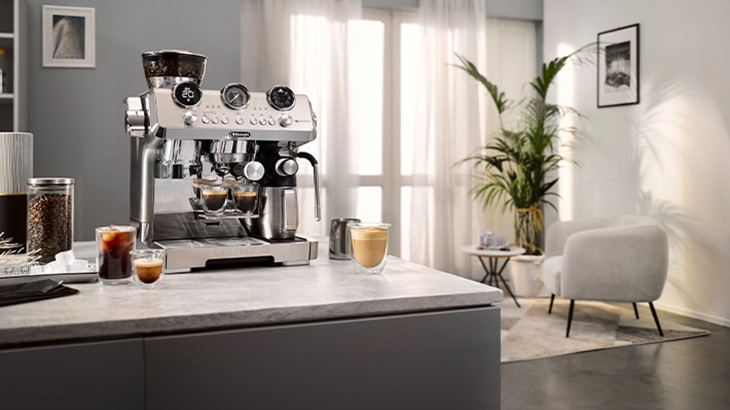 Moderne Siebträgermaschine auf einer Kücheninsel, umgeben von frisch zubereiteten Kaffees in einem hellen, stilvollen Wohnraum.