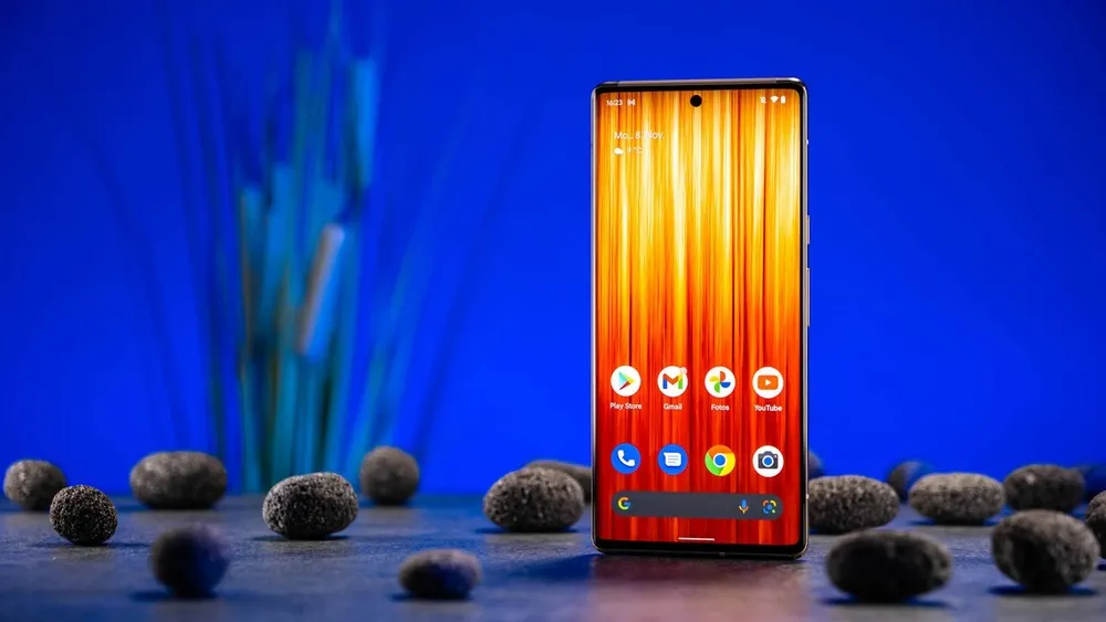 Ein Google Pixel 6 Pro, auf dem der Android-Homescreen zu sehen ist, steht auf einem Tisch vor blauem Hintergrund.