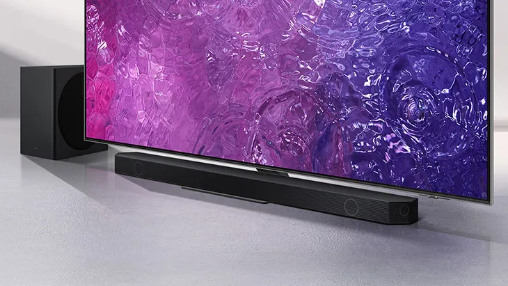 Ein Fernseher mit lila Bildschirm steht auf einem grauen Untergrund, neben einer Soundbar und einem Subwoofer.