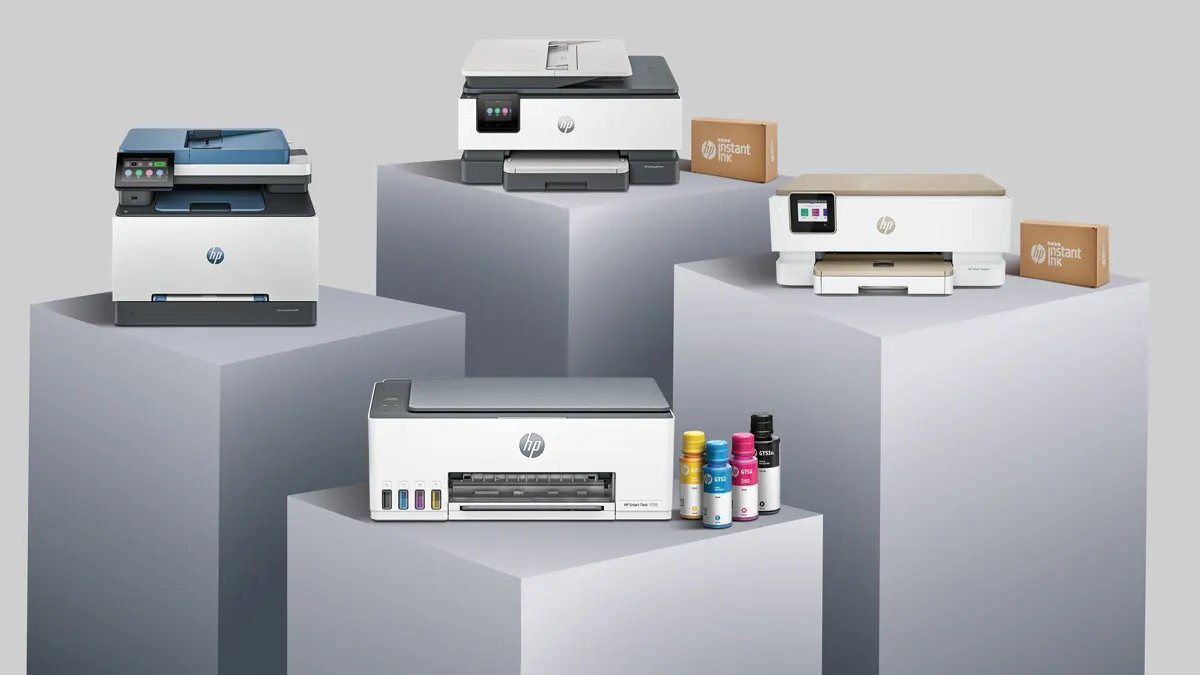 Mehrere weiße HP-Drucker stehen auf grauen Sockeln mit Tintenflaschen und Instant-Ink-Boxen.