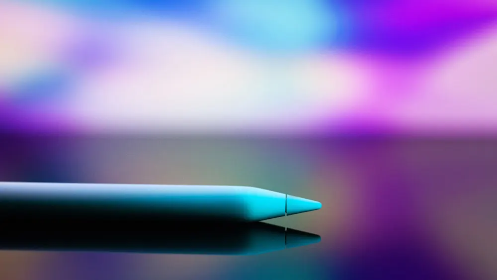 Ein türkisfarbener Stift liegt auf einer reflektierenden Oberfläche vor einem verschwommenen, farbenfrohen Hintergrund in Lila und Weiß.