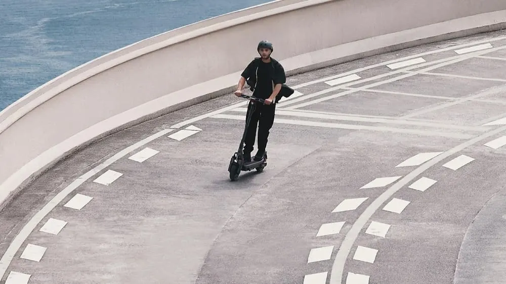 Fahrer mit Helm fährt mit dem SEGWAY Ninebot MAX G3 D E-Scooter auf breiter geschwungener Rampe am Wasser.