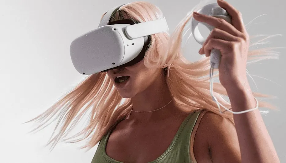 Eine Person mit einem Headset und einem Controller vor einem hellen Hintergrund. Die Person trägt ein grünes Top und eine Halskette.