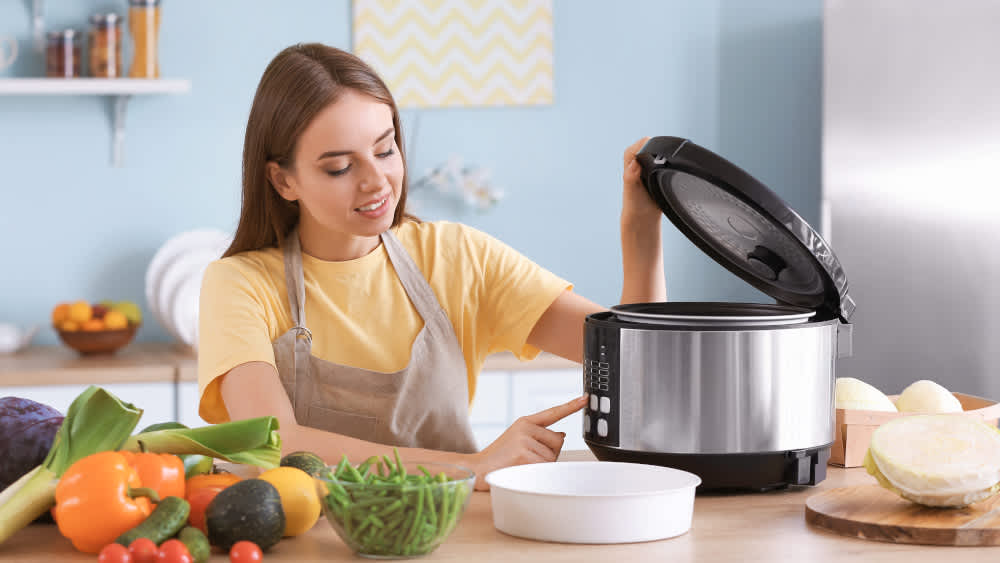 Eine Frau steht in einer Küche und benutzt eine Küchenmaschine mit Kochfunktion / Multikocher