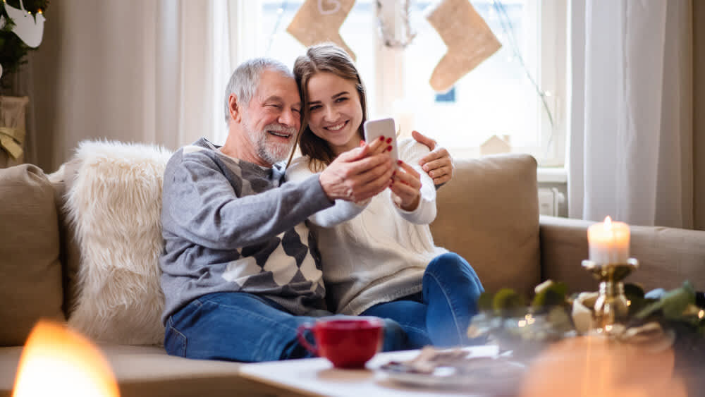 Ein Mann und seine Enkeltochter sitzen gemeinsam auf einem Sofa und machen ein Selfie.