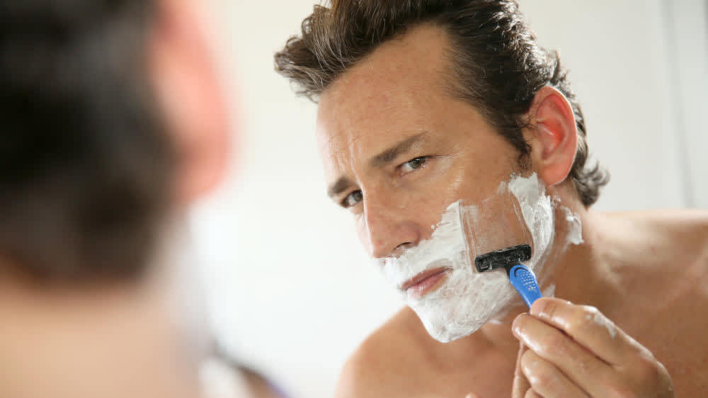 Ein Mann steht vor einem Spiegel und rasiert sich.