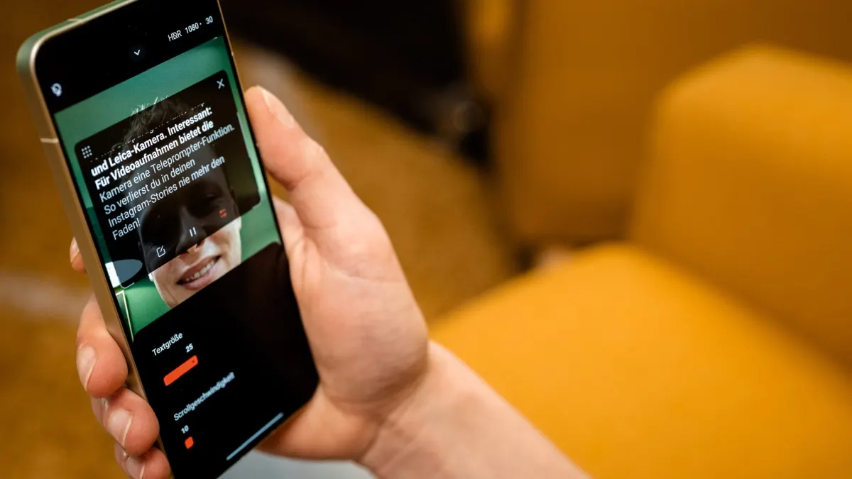 Eine Hand hält ein Smartphone mit einer Teleprompter-App. Textgröße und Scrollgeschwindigkeit sind einstellbar. Der Hintergrund ist gelb.