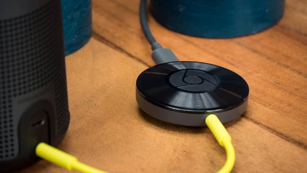 Google Chromecast-Audiogerät mit gelbem Kabel, das zu einem Lautsprecher führt