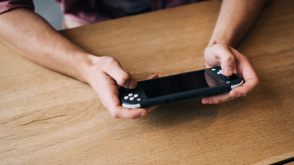 Ein Mann benutzt am Tisch eine Nintendo Switch Lite.