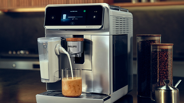 Der Milchaufschäumer der Philips Café Aromis füllt Milch in ein Glas mit Kaffee.