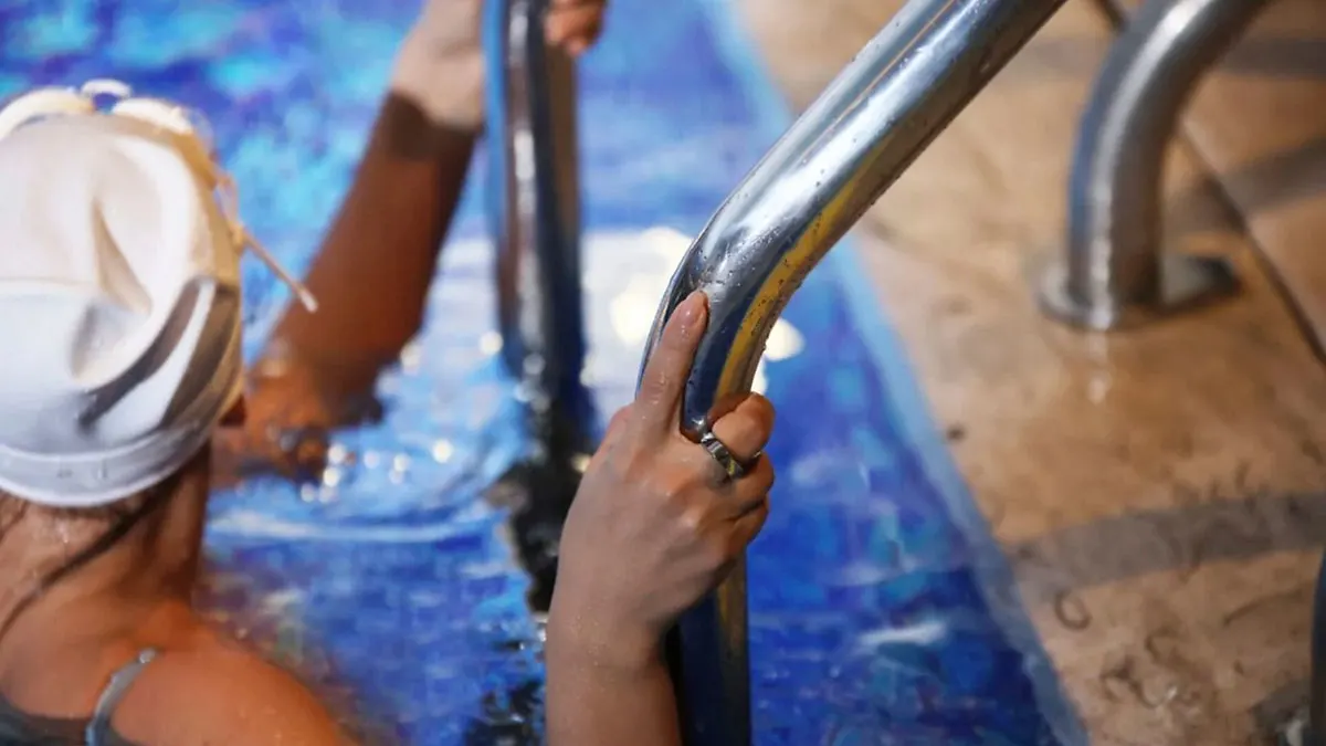 Eine Frau in Badekleidung trägt einen Smart-Ring am rechten Mittelfinger und steigt aus einem Schwimmbecken.