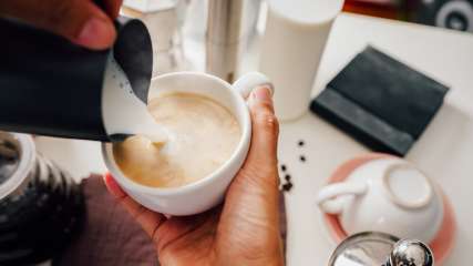 Eine Person gießt Milch in eine Kaffeetasse.