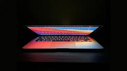 Ein geöffneter Laptop steht auf einem dunklen Tisch, der Bildschirm zeigt eine farbenfrohe Anzeige.