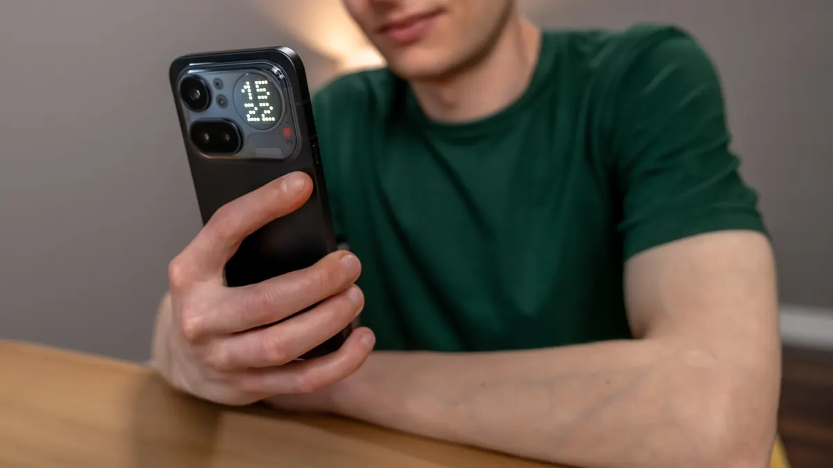 Alex sitzt auf einem Tisch und blickt auf das Nothing Phone (4a) Pro, das er in der Hand hält.