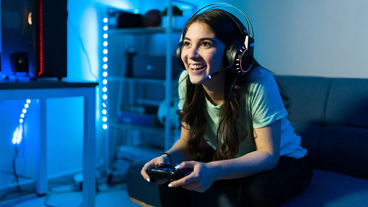 Lachende Frau mit Headset hält einen Controller im blau beleuchteten Raum.