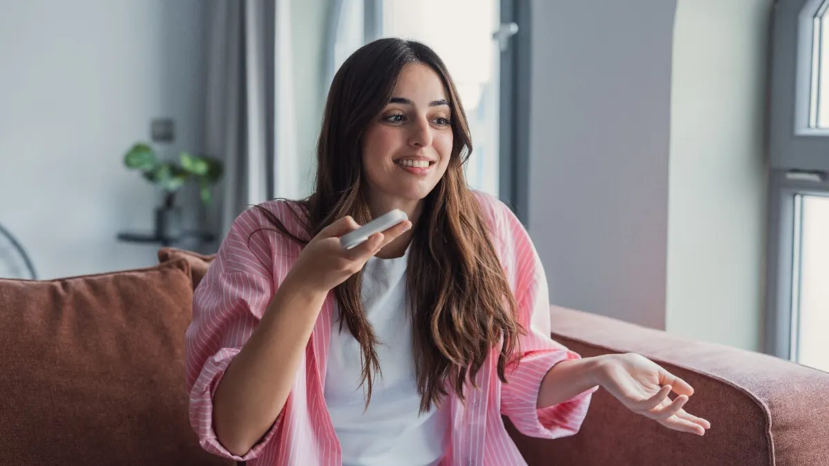 Eine Frau sitzt auf dem Sofa und spricht in ihr Smartphone.