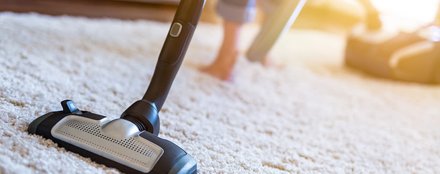 Eine Person saugt einen weißen Teppich mit einem Staubsauger.