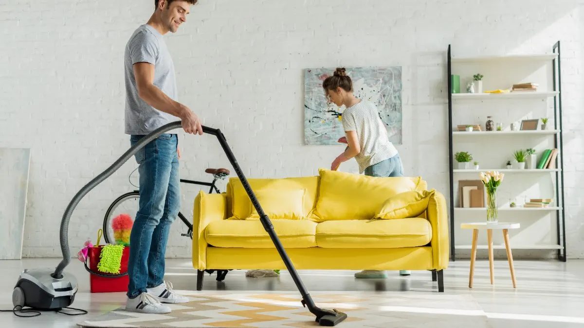 Ein Mann und eine Frau reinigen ein Wohnzimmer mit Staubsauger und Wischmopp.