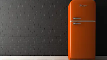 Ein orangefarbener Retro-Kühlschrank steht rechts vor einer grauen Ziegelwand und einem hellen Boden. Er hat zwei silberne Griffe.