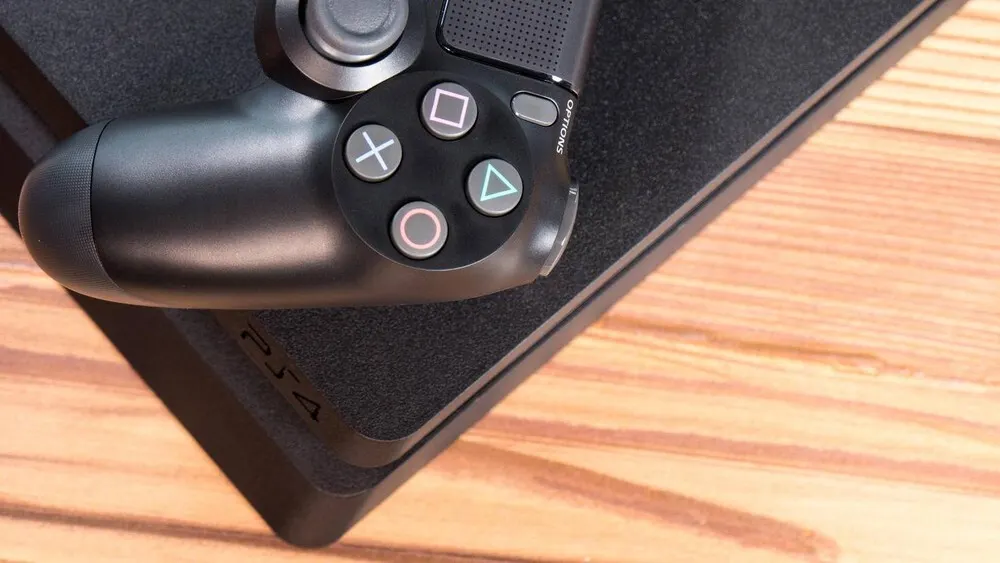 Ein schwarzer PlayStation-Controller liegt auf einer schwarzen Konsole auf einem Holztisch.