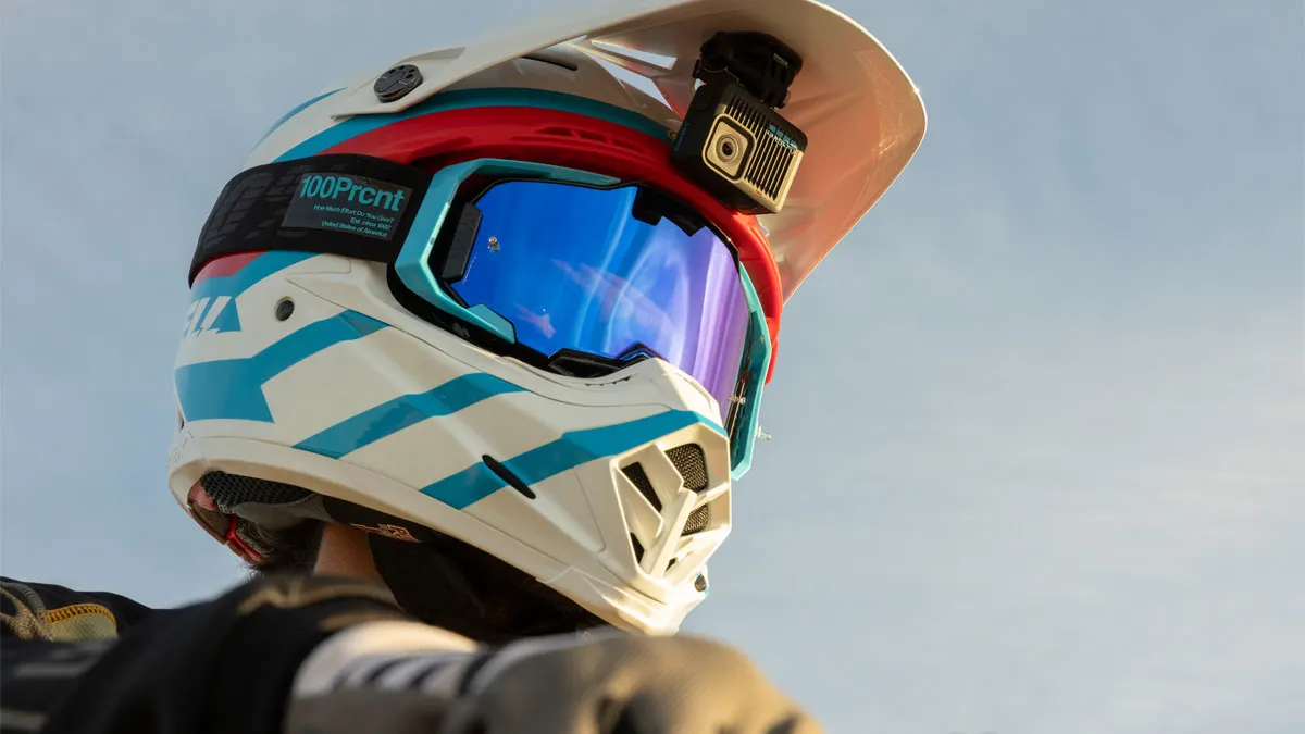 Nahaufnahme eines weißen Helms mit blau gestreiften Akzenten, blauer Brille und montierter Kamera vor blauem Himmel.