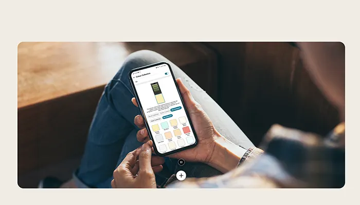 Eine Person hält ein Smartphone mit einer Farbauswahl-App in den Händen, vor Jeansstoff.