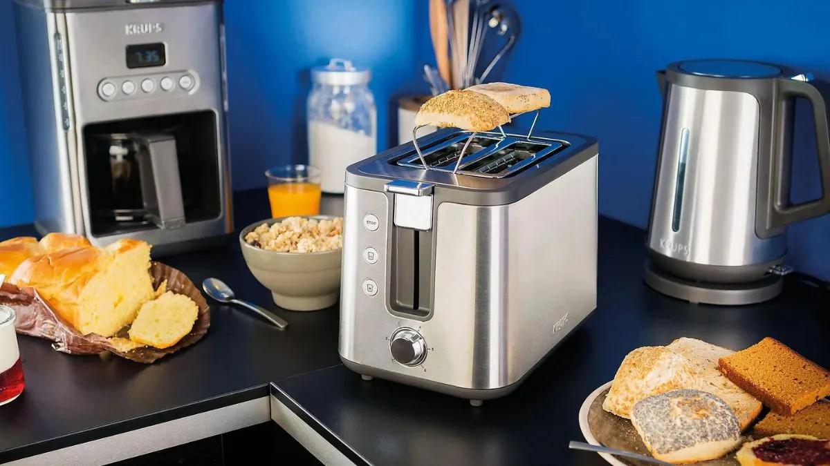 Der Toaster Krups KH442D steht auf einer Küchenarbeitsfläche zwischen anderen Küchengeräten und toastet ein Brötchen.