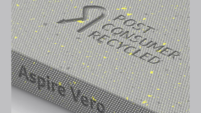 Auf grauem Stoff sind die Worte "Post Consumer Recycled" und ein Logo eingeprägt. Gelbe Punkte sind auf dem Stoff.