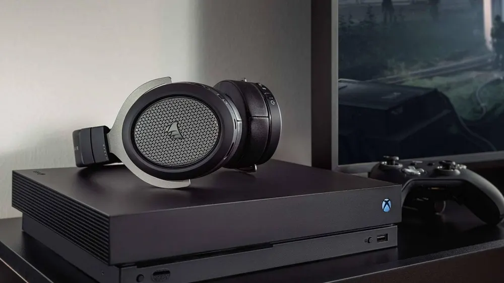 Schwarzes Headset auf einer schwarzen Xbox-Konsole, daneben ein Controller vor einem verschwommenen Bildschirm.