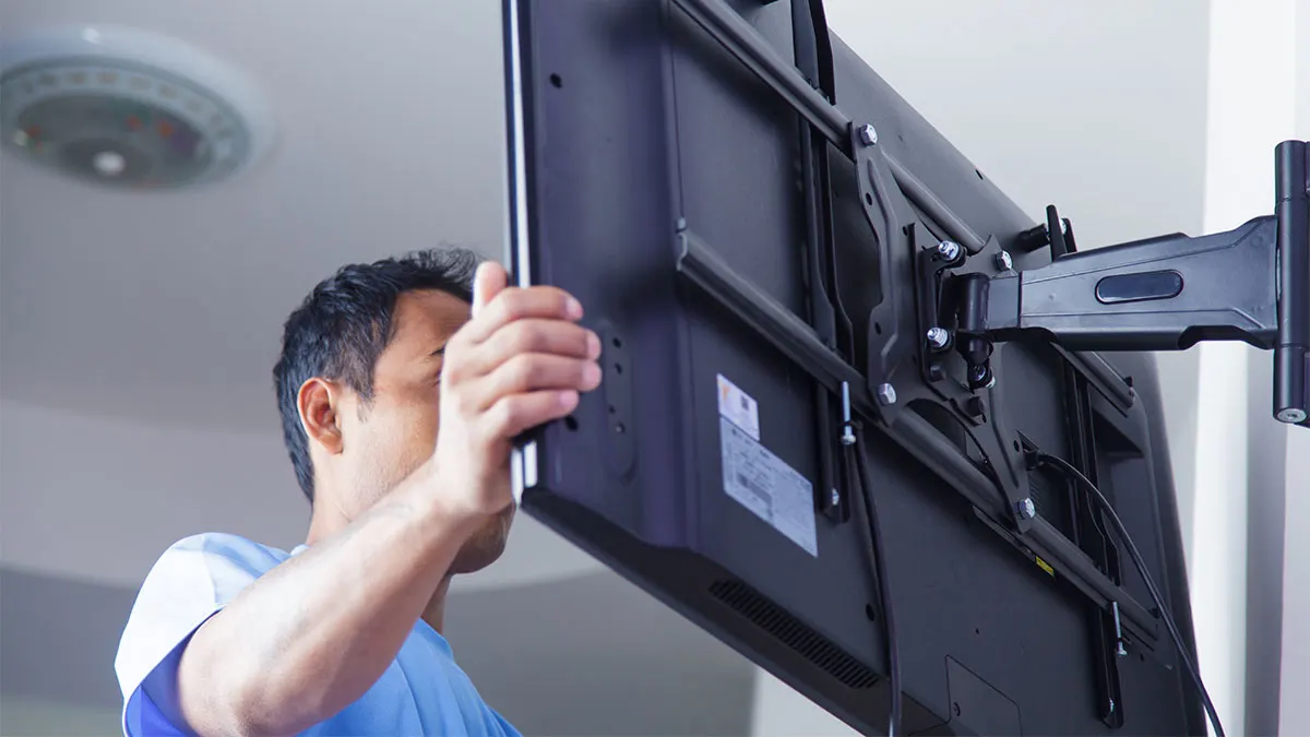 Ein Mann montiert einen schwarzen Flachbildfernseher an einer beweglichen Wandhalterung.