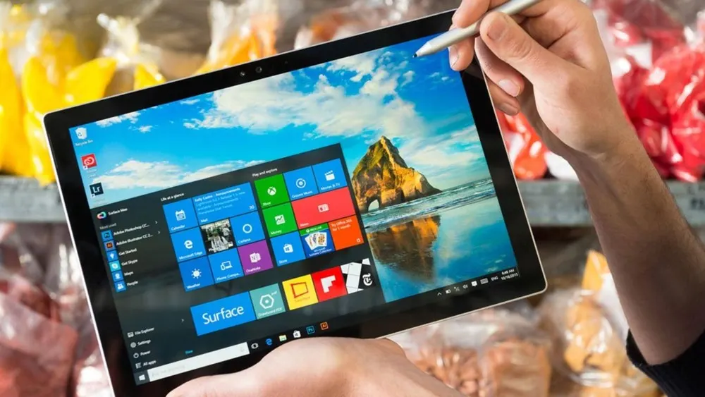 Eine Person hält ein Tablet mit einem Stift in der Hand. Auf dem Bildschirm sind Apps und ein Hintergrund mit einem Felsen zu sehen.