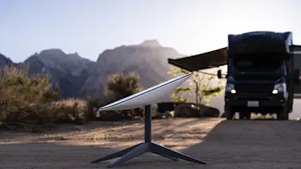 Eine Starlink-Antenne steht in der Natur vor einem Wohnmobil.