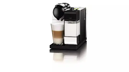 Eine Kaffeemaschine mit Milchaufschäumer steht neben einem Glas Latte Macchiato auf einer schwarzen Unterlage.