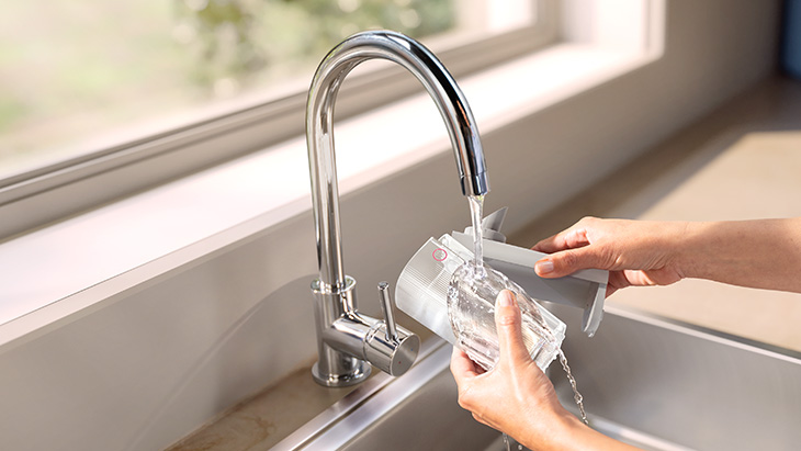 Eine Hand wäscht den Milchaufschäum-Behälter der Philips Café Aromis unter dem fließenden Wasserhahn ab. 