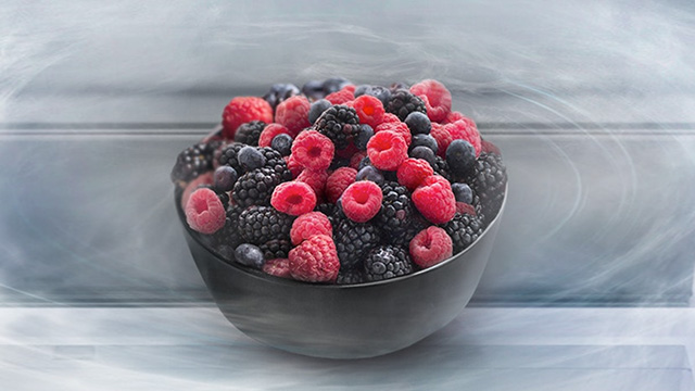 Eine Schale enthält Himbeeren, Brombeeren und Blaubeeren vor einem verschwommenen, hellgrauen Hintergrund.