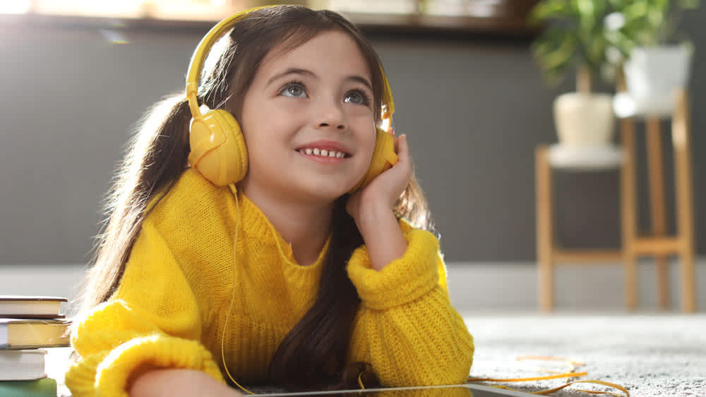 Ein Mädchen in einem gelben Pullover hört Musik auf gelben Kinderkopfhörern.