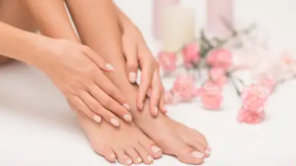 Beine und Hände auf weißem Grund, dekoriert mit rosa Blumen und Flaschen im Hintergrund.