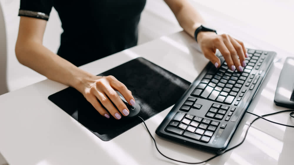 Eine Frau bedient eine Maus und Tastatur mit ihren Händen.