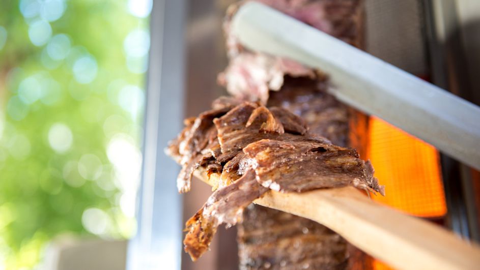 Kebap-Fleisch wird mit einer Zange in die Kamera gehalten.