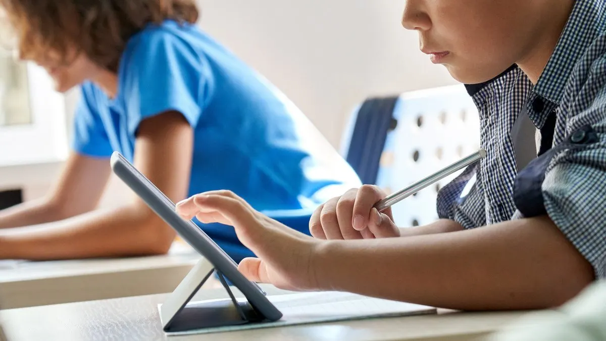 Ein Schulkind bedient ein Tablet mit einem Stylus in der Hand.