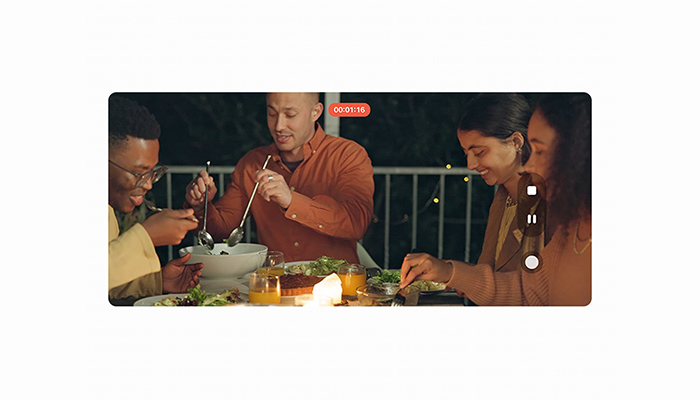 Vier Personen sitzen abends gemeinsam am Tisch und essen. Im Vordergrund zeichnet ein Smartphone ein Video der Szene auf.