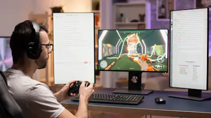 Ein Mann mit Kopfhörern spielt ein Videospiel an einem Schreibtisch mit drei Bildschirmen, einer Tastatur und einer Maus.