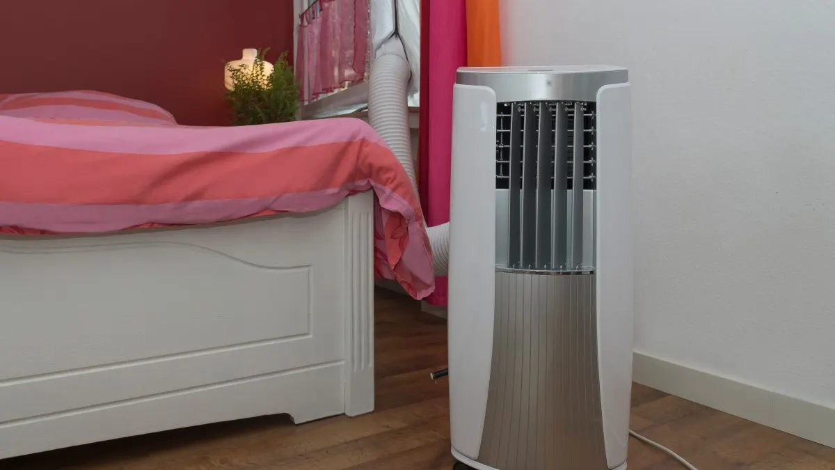 Ein Schlafzimmer mit einem weißen Bett mit rot-rosa Bettwäsche und einer tragbaren Klimaanlage.