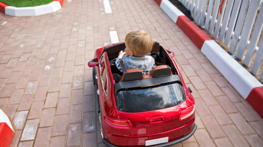 Junge fährt rotes Elektro-Kinderauto auf Straße für Kinder