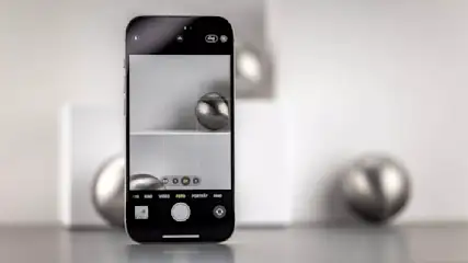 Ein Smartphone zeigt einen Bildschirm mit einer Kameraansicht. Zwei silberne Kugeln sind auf einem weißen Regal zu sehen.