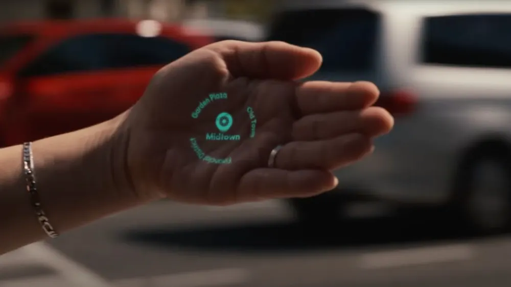 Eine Hand hält eine holografische Karte mit der Aufschrift Midtown, Garden Flats und Old Town, mit Autos im Hintergrund.